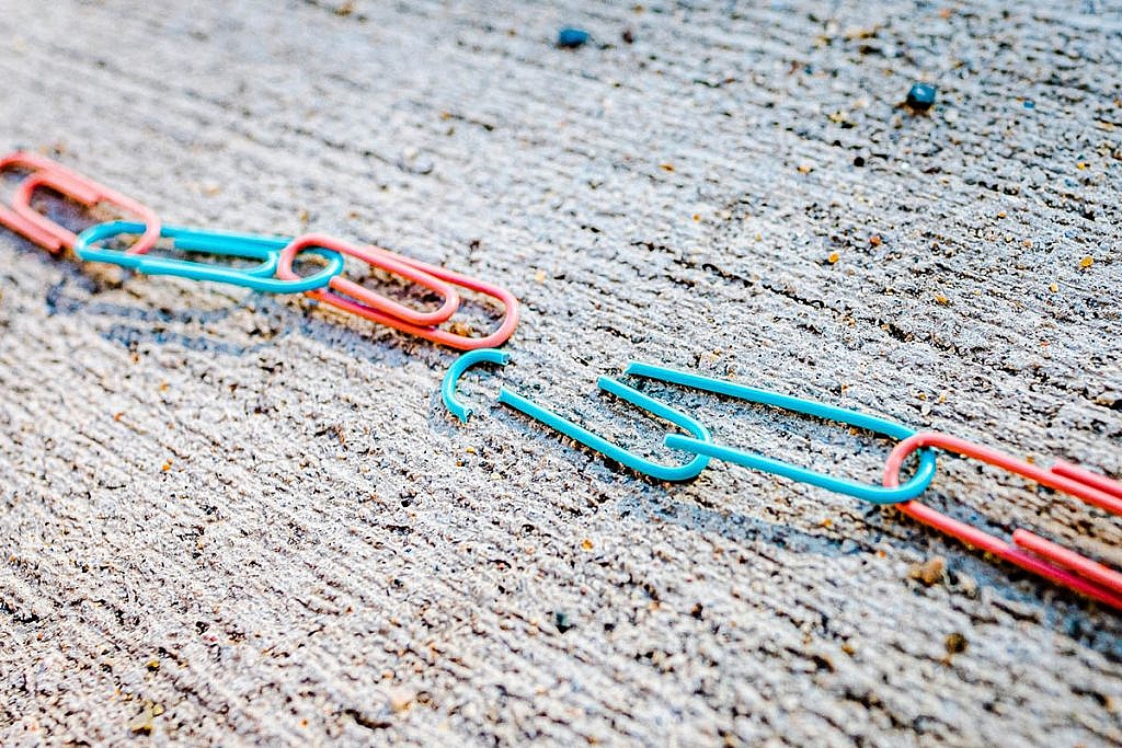clipes de papel nas cores azul e rosa presos um no outro. um dos clipes está quebrado e rompe o elo.
